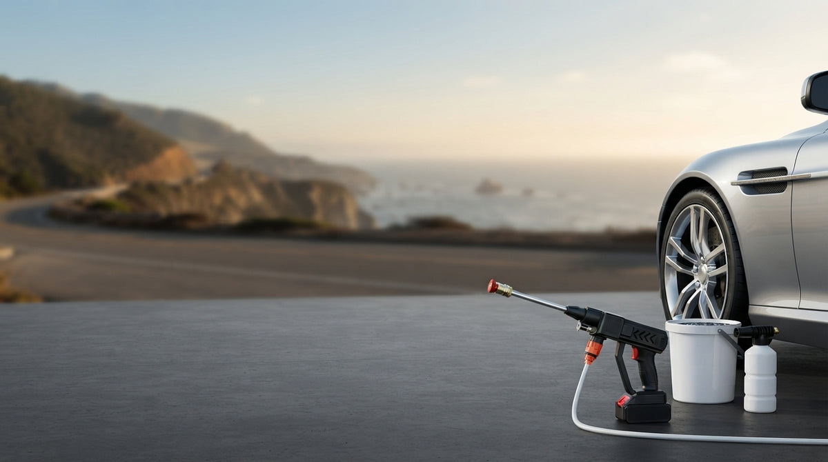 A cordless high-pressure car wash spray gun on a driveway at a coastal location with a luxury car partially visible.